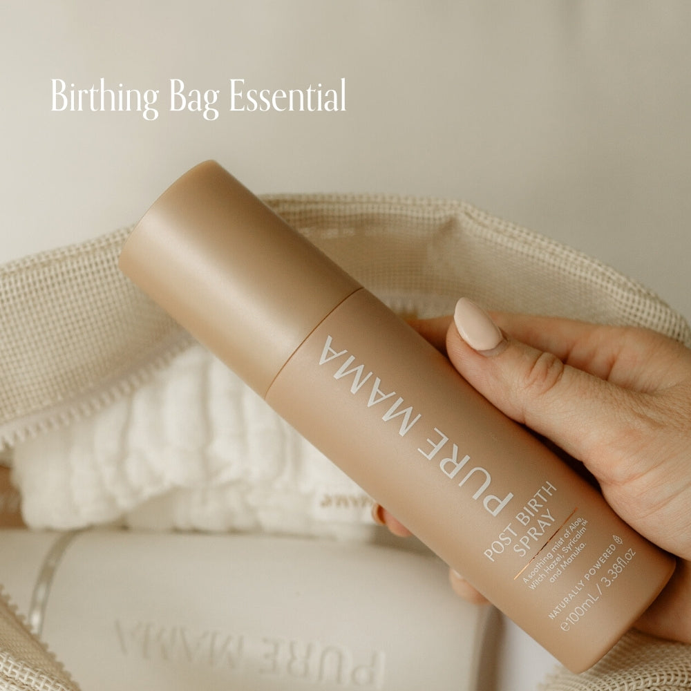 A hand holds a bottle of Pure Mama NZ Post Birth Relief Spray above an open bag with a towel inside. “Birthing Bag Essential” appears in the upper left corner.