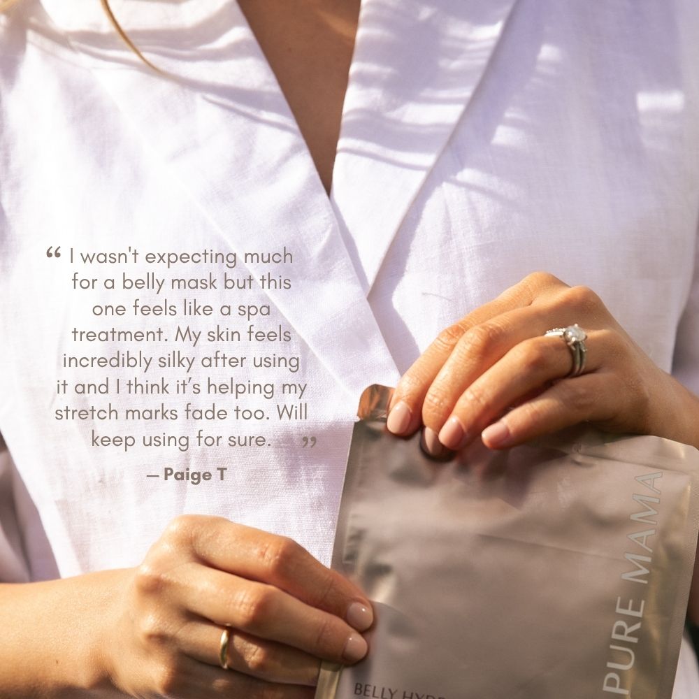 A person in a white robe holds a silver Pure Mama NZ Belly Hydration Mask, with a testimonial about the mask’s hydrating effects on skin and stretch marks shown beside them. Their wedding and engagement rings are visible.