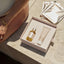 A person sits on a light stone surface next to an open Pure Mama NZ Belly Spa Kit, featuring a dropper bottle, tube, and two shiny sheet masks—including a belly hydration mask. Gold jewelry adorns their arm.