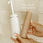 A hand holds a white Peri Wash Bottle and another holds a tan Pure Mama NZ Post Birth Relief Spray against a tiled background. Text: Pair with the Peri Wash Bottle for gentle postnatal healing.